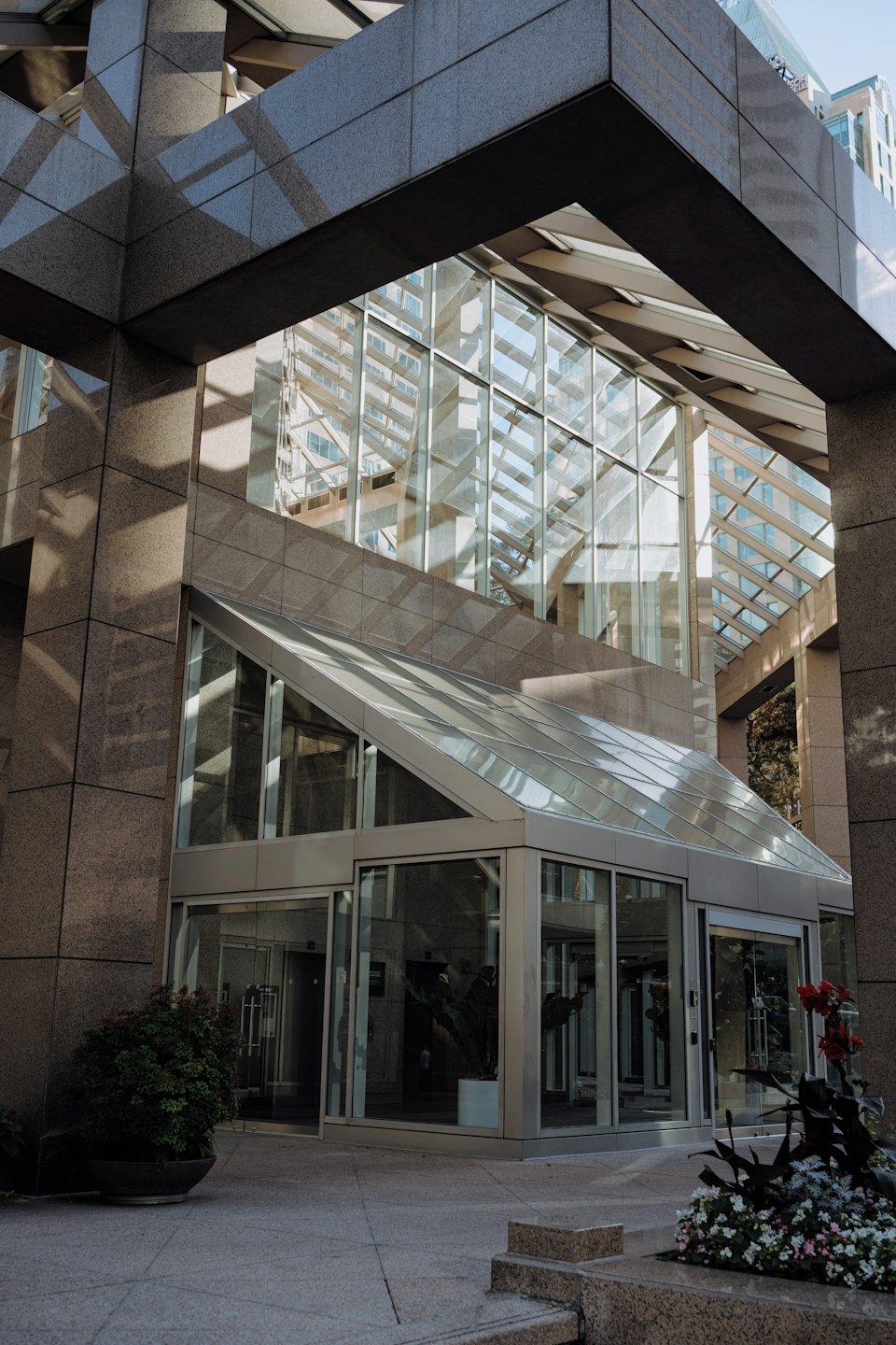Modern glass building entrance with stone walls and plants.